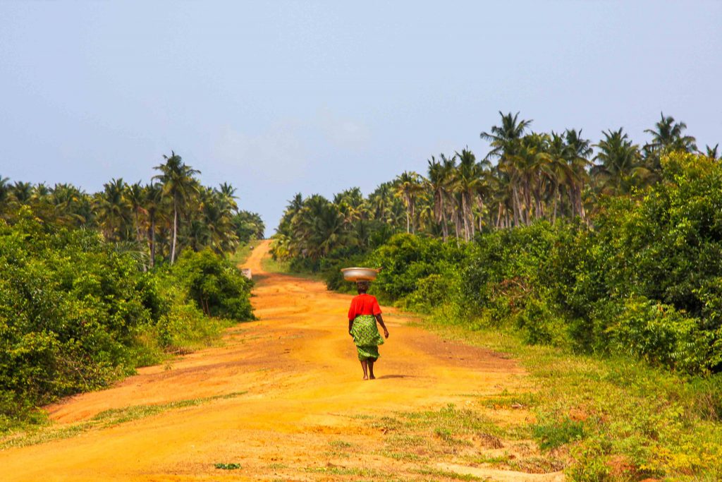 African woman walking on a long red ochre dirt road in Togo, a great destination for your first time in Africa